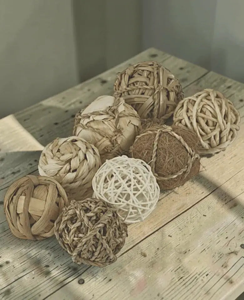 A group of decorative woven rope balls in natural beige, brown, and white tones arranged on a rustic wooden tabletop.